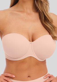 Světle růžová bezramínková podprsenka s hladkými, tvarovanými košíčky, boční podporou a jemným středovým švem, která má malý dekorativní stříbrný detail.