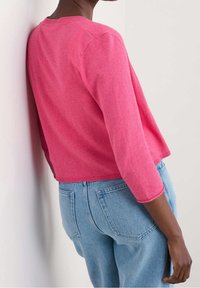 Růžový pletený svetr s třičtvrtinovými rukávy, žebrovaným výstřihem a volným střihem, spojený se světle modrými džínov�ými kalhotami.