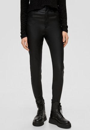 Pantalons noirs taille haute en simili cuir avec une finition lisse et une silhouette ajustée, associés à des bottes plateformes à lacets noires.