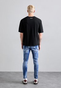 Camiseta negra de manga corta, combinada con jeans de mezclilla azules desgastados que presentan salpicaduras de pintura blanca. Zapatillas con suela blanca y acentos coloridos.