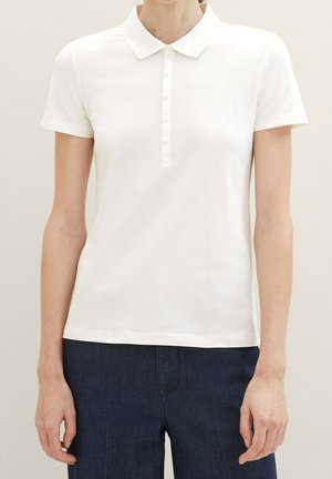 Bílá polokošile s krátkým rukávem a plochým límečkem, s knoflíkovou légou a hladkou, ribbed texturou. Nošena s tmavými džíny.