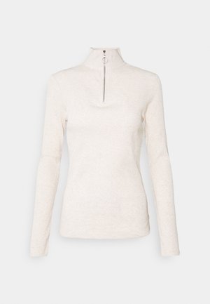 Top de manga larga de color crema con cuello alto, que presenta una media cremallera, hecho de una tela suave y texturizada. Diseño simple y minimalista.