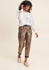 Metallic bronzefarbene Hose mit lässiger Passform und Kordelzugbund, kombiniert mit einem hellgrauen Pullover mit floralem Muster.