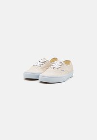 Zapatillas de lona en beige claro con cordones blancos, suelas de goma y punta redonda; cuentan con una etiqueta en el lateral y material texturizado.
