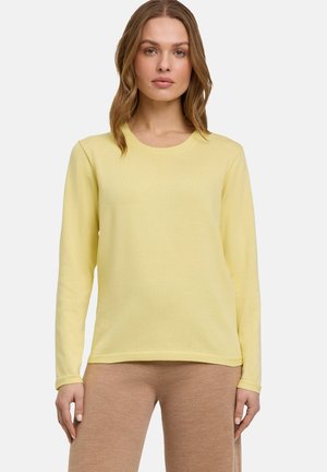 Maglietta a maniche lunghe di colore giallo chiaro, scollatura rotonda, morbido al tatto, abbinata a pantaloni beige. Design semplice senza motivi o dettagli visibili.
