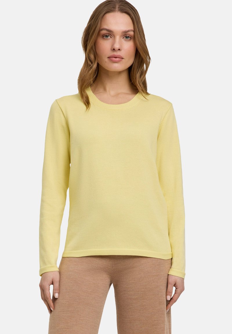 Langsleeve top in lichtgeel, ronde halslijn, zachte textuur, gecombineerd met beige broek. Eenvoudig ontwerp zonder zichtbare patronen of accenten.