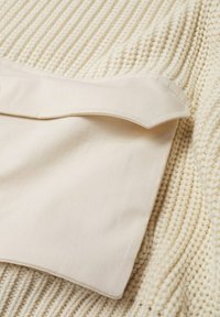 Beżowa dzianina prążkowana z gładkim, kremowym mankietem nachodzącym na nią. Teksturowana powierzchnia z widocznym przeszyciem i zaokrąglonymi krawędziami mankietu.