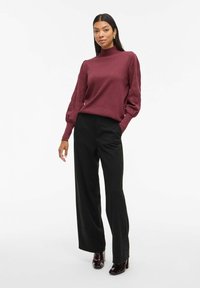 Ribbed turtleneck bourgogne avec des manches ballon, associé à un pantalon noir à jambes larges et des talons noirs brillants. Texture lisse, design simple.