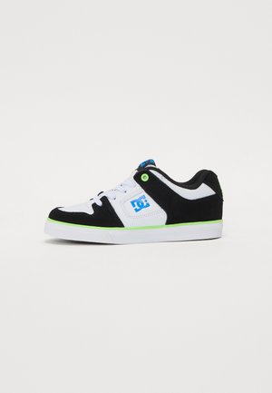 Zapatilla baja en negro y blanco con logo azul, ojal verde y ribete en la suela, cordones blancos y cuello acolchado, vista lateral.