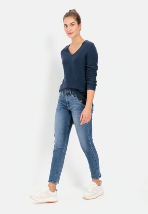 Marineblauer V-Ausschnitt-Pullover, kombiniert mit hellblauen, eng anliegenden Jeans und weißen Sneakers. Der Pullover hat lange Ärmel und eine weiche Textur.