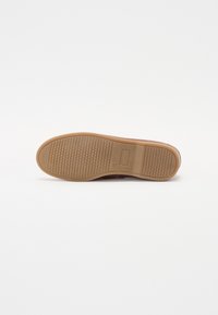 Braune Schuhsohle mit einem strukturierten Gummiboden und dem eingravierten "bugatti"-Logo in der Mitte auf einem weißen Hintergrund.
