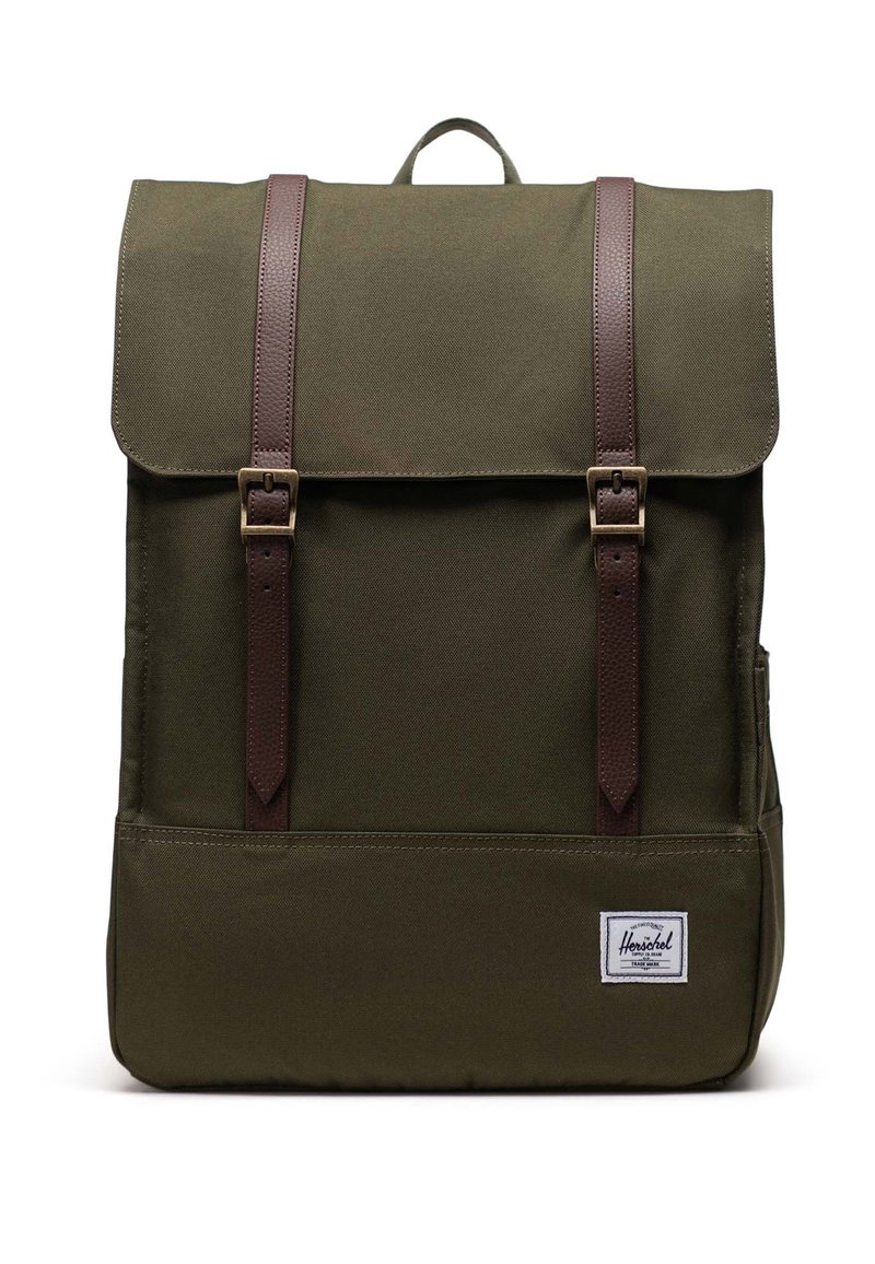 Oliiviv roheline seljakott volditava klapiga, pruuni nahkrihmade ja messingist tarvikutega. Omab esipocketit ja valget logo sildi.