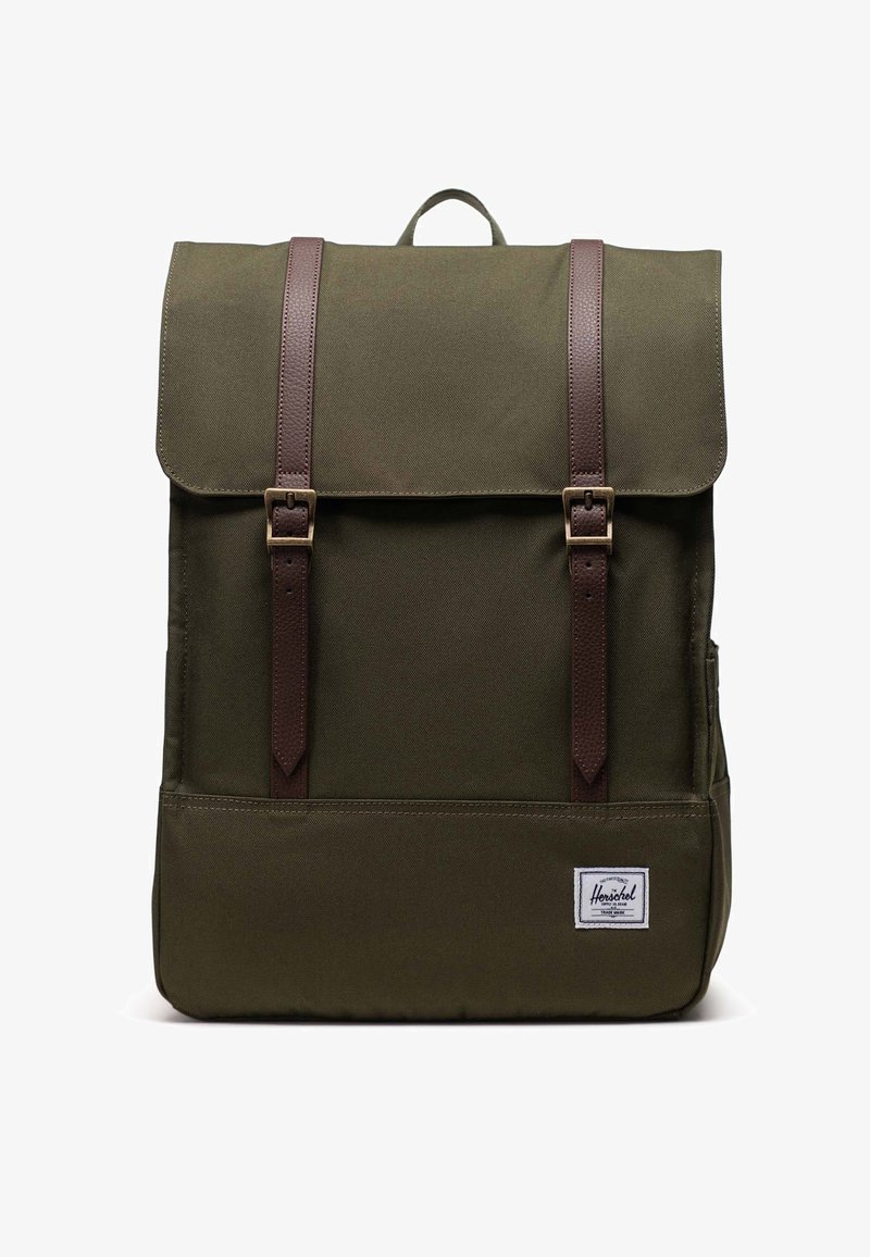 Oliiviv roheline seljakott volditava klapiga, pruuni nahkrihmade ja messingist tarvikutega. Omab esipocketit ja valget logo sildi.