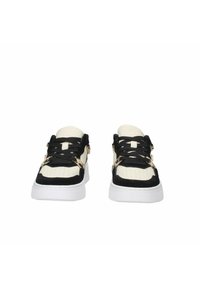 Sneaker neri e crema realizzati in materiali scamosciati e in pelle, con suola piatta in gomma bianca, lacci neri e dettagli forati sulla punta. Accenti dorati vicino ai lacci.