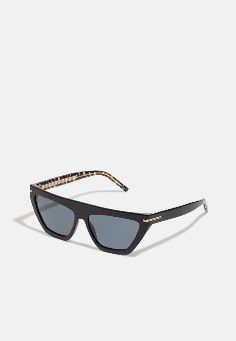 Black sunglasses with triangular lenses, gold accents, and textured, patterned temple arms. Matte finish and dark gray lenses.
