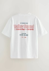 Tricou alb cu mânecă scurtă, cu text roșu și albastru "Valley Sound Crimson Ridge Shelbyville" și un număr de telefon fictiv imprimat pe spate.