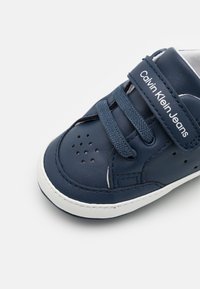 Granatowe skórzane buty z białą podeszwą, z perforacjami, sznurowadłami i rzepem. Logo "Calvin Klein Jeans" nadrukowane na rzepie.