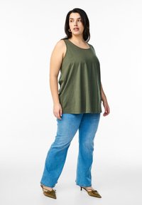 Olijfgroen mouwloze top met een ronde halslijn, gecombineerd met lichtblauwe denim jeans en olijfgroene pumps met een spitse neus.