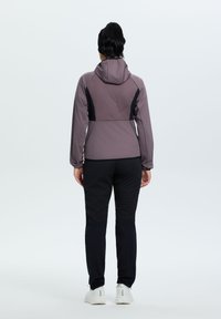 Giacca da donna per esterni in mauve con accenti neri, dotata di cappuccio, pannello posteriore testurizzato e pantaloni neri aderenti con gambe affusolate.