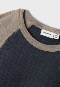 Donkerblauwe en lichtbeige T-shirt met een geribbeld textuur, contrasterende raglan mouwen en een gestikte halslijn. Bevat merklabel.