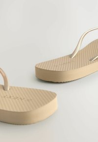 Bežid sandaalid tekstureeritud tallade ja õhukeste rihmadega, millel on pehme jalatugi ja ümar varvaste ala. Üldiselt sile pind.