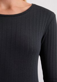 Schwarzes, geripptes Langarmoberteil mit rundem Ausschnitt. Der Stoff hat eine weiche Textur und vertikale Streifen, die ein figurnahes Design betonen.