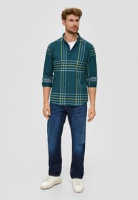 Teal geruite overhemd met gele lijnen, lange mouwen opgerold bij de cuffs, gedragen over een wit t-shirt, gecombineerd met blauwe jeans en witte sneakers.