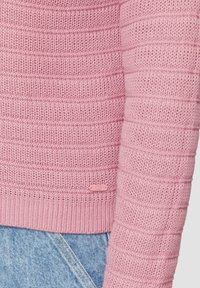 Pull en tricot rose avec un design texturé et côtelé, orné de rayures horizontales. Une petite étiquette QS est visible près de l'ourlet.