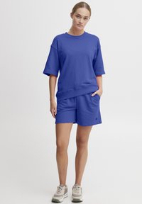 T-shirt surdimensionné en mélange de coton bleu à manches courtes, associé à un short bleu assorti avec poches latérales. Des baskets complètent le look.
