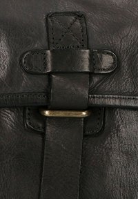 Detalle de bolsa de cuero negro con una correa prominente y un hebilla de latón, superficie texturizada y costuras en contraste.