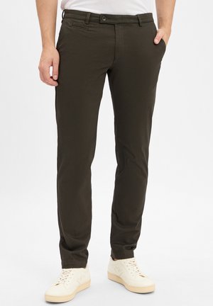 Dunkelgrüne, figurbetonte Hose mit glatter Textur, mit Fronttaschen und Knopfverschluss. Kombiniert mit hellbeigen Sneakers.