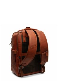 Sac à dos en cuir marron avec une forme structurée, des accents en mesh et des bretelles réglables. Il dispose d'une poche latérale et d'une poignée supérieure pour le transport.