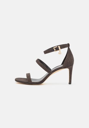 Brązowy sandał na obcasie z odkrytymi palcami, posiadający dwie równoległe paski oraz pasek wokół kostki; materiał o fakturze, złota klamra i smukły obcas.
