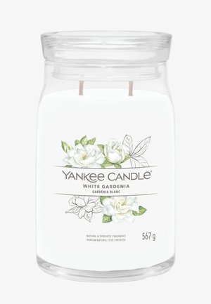 Duidelijke glazen potkaars met twee lonten, gelabeld "Yankee Candle White Gardenia" met een ontwerp van witte gardenia bloemen en groene bladeren.