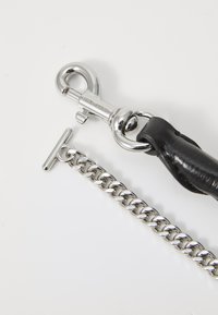 Must õhuke must nahkrihm metallklambriga, millel särav hõbehelmed ja T-kujuline lukk, valge tausta ees.