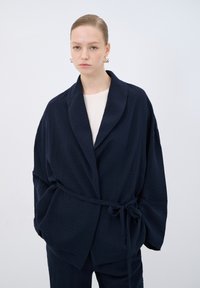 Navy kimono jacket in textured fabric with a shawl collar and tied waist. Loose fit with wide sleeves and minimal detailing.