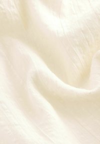 Tissu léger de couleur crème avec une surface douce et texturée et de subtils plis, indiquant un matériau naturel et respirant.