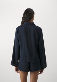Mörkblå skjorta med långa ärmar och krage, tillverkad av ett slätt tyg, i kombination med matchande shorts, minimal design, inga synliga mönster.