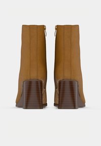 Pár világosbarna velúr bokacsizma rakott fakeretes sarokkal, hátulnézet fehér háttéren.