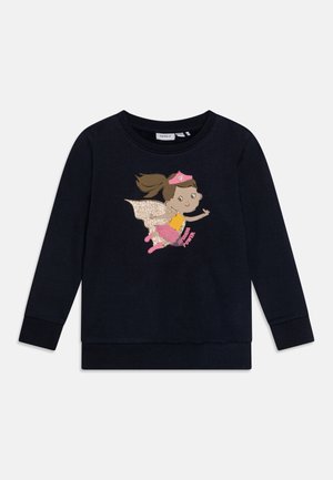 Navyblå langærmet skjorte med grafik af en flyvende pige-superhelt, der bærer en pink hat, kappe, støvler og ordene "Superhelt styrke."