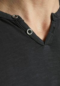 Sort henley skjorte med knaplukning og metalknapper, tekstureret stof og et diskret meleret mønster.
