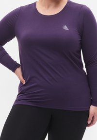 Paarse sportieve top met lange mouwen, gemaakt van gladde, rekbare stof. Heeft een subtiel logo op de linkerkant van de borst en een ronde halslijn.