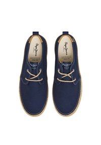 Scarpe in tela blu navy con punta rotonda, lacci beige, texture tessile intrecciata e suola color tan a contrasto. Logo sulla soletta e piccola etichetta sul tallone.