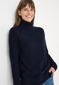 Pull à col roulé bleu marine en tissu doux, avec des accents côtelés au niveau du col et des poignets, et une coupe décontractée.