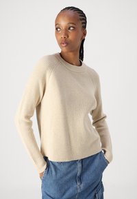 Μπεζ ριμπ πλεκτό πουλόβερ με στρογγυλή λαιμόκοψη και μακριά μανίκια, συνδυασμένο με τζιν φούστα, που διαθέτει άνετη εφαρμογή και απαλή υφή.