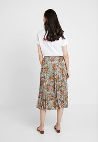 Blommig kjol med veck, med ett mönster i vitt, grönt och orange på svart botten. Kombineras med en vit t-shirt och sandaler.