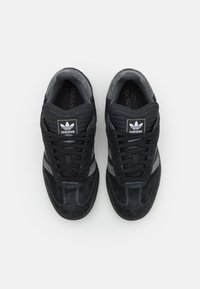 Čierne semišové športové topánky so sivými akcentmi, textúrovaný povrch, okrúhla špička, čierne šnúrky a logo Adidas na jazyku a boku.