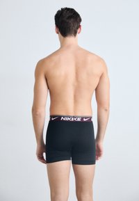 Crne bokserice s bordo pojasom s Nike oznakom. Tkanina izgleda glatko s prilagođenim dizajnom, prikazane iz stražnjeg pogleda.