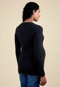 Hosszú ujjú fekete bordázott kismama póló, testhez álló fazon, finom rugalmasság, kerek nyakkivágás, világoskék farmernadrággal párosítva, hátulról nézve.