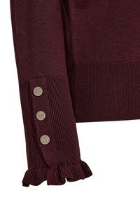 Vinröd stickad tröja med ribbad mudd och tre dekorativa guldknappar samt en volangnederdel. Slät textur, figurnära design.